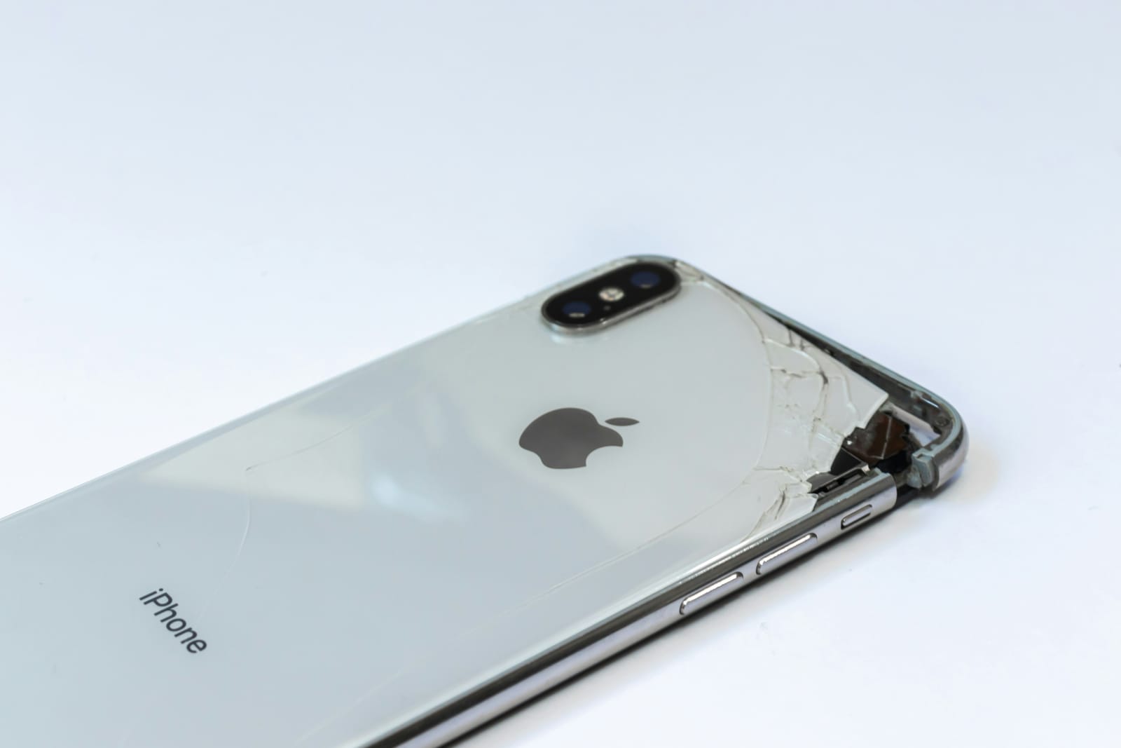 The rear of a silver iPhone with its back glass badly cracked