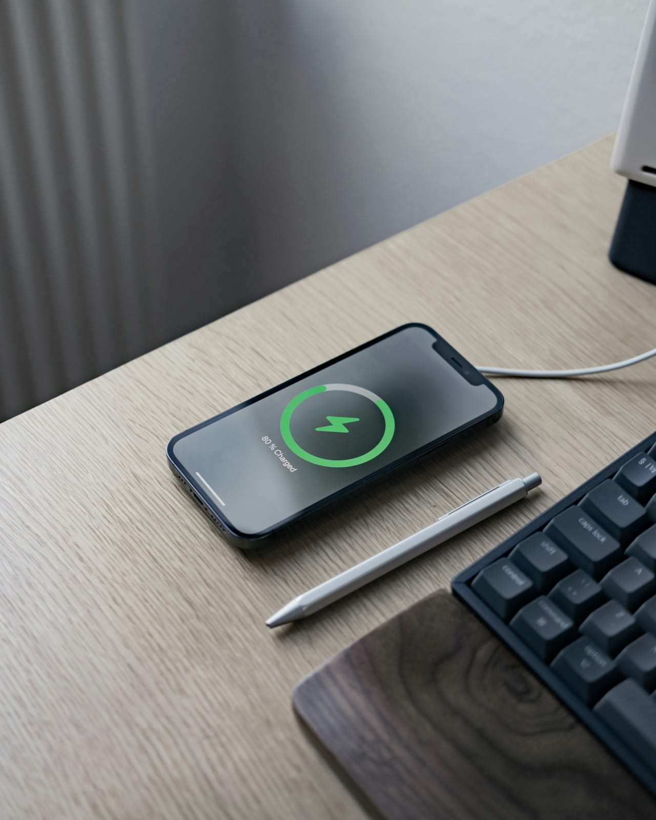 An iPhone charging on a desk, its screen showing 80 percent charged