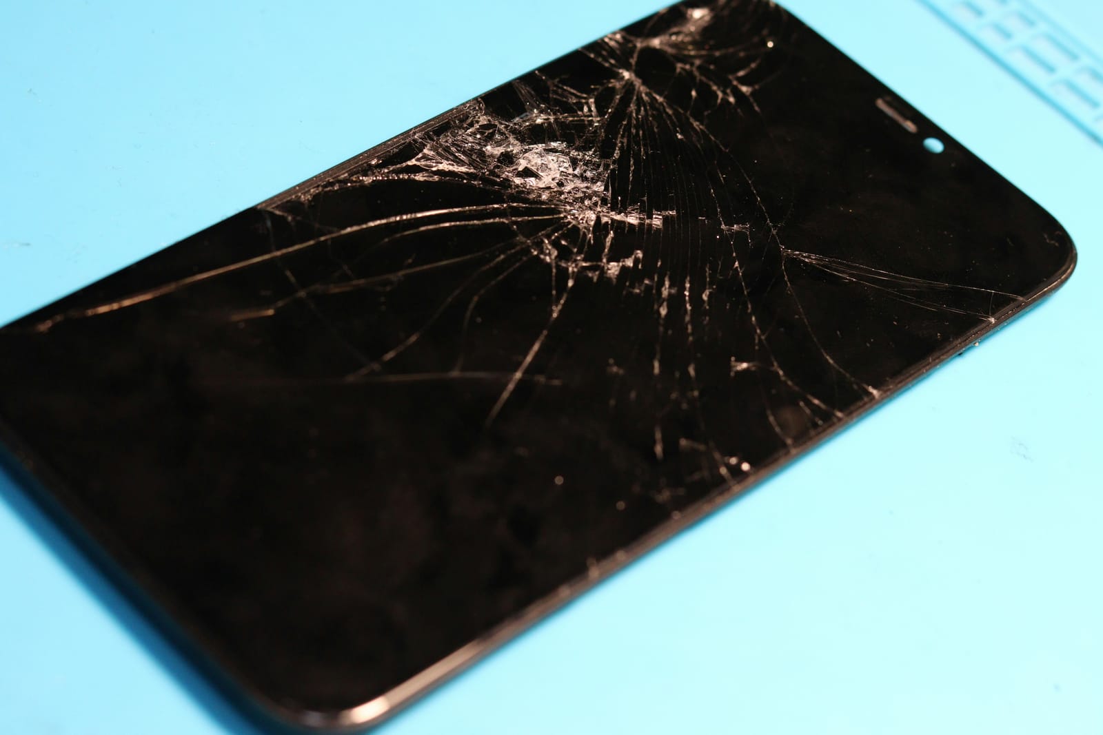 A smartphone with a badly cracked and shattered screen on a repair mat
