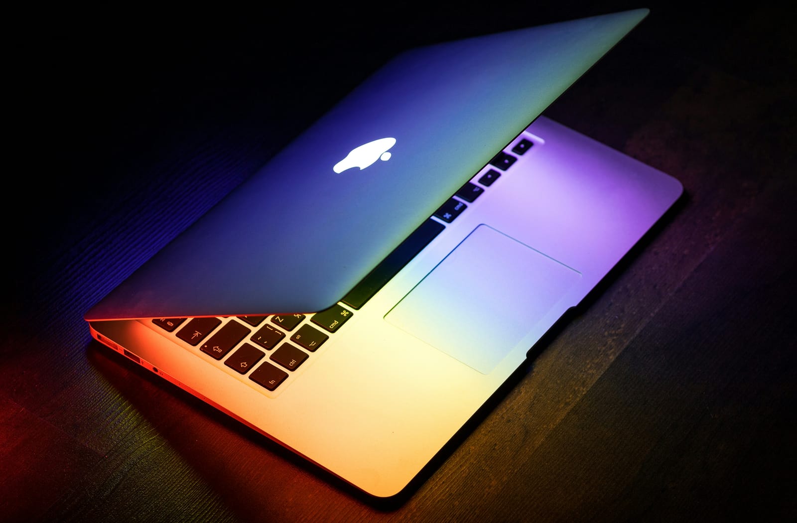 A MacBook part-open in a dark room with its Apple logo glowing