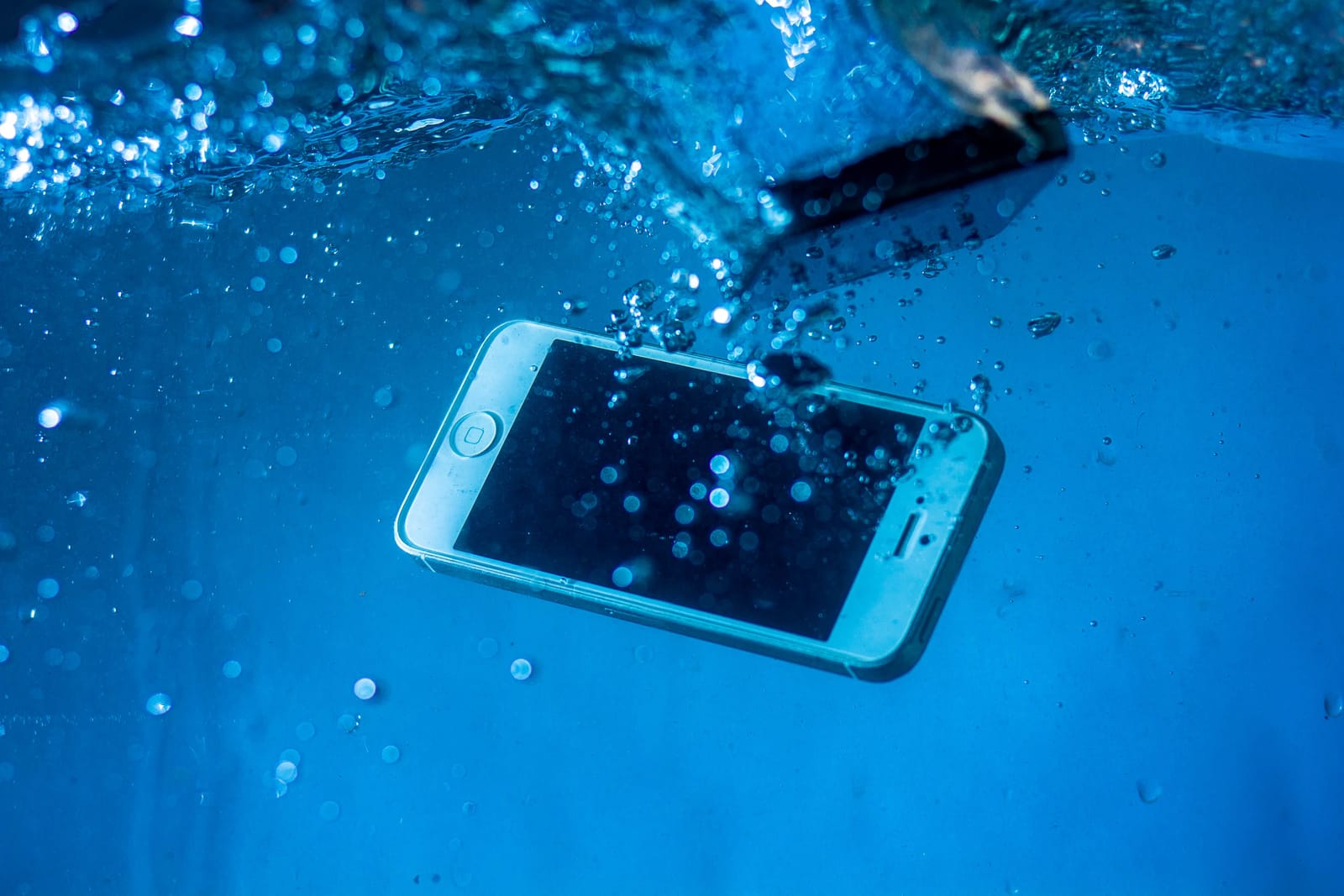 A smartphone sinking underwater with air bubbles, moments after being dropped in water